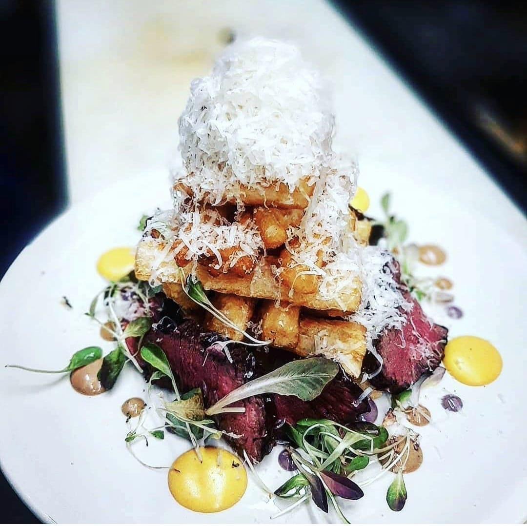 Sliced steak topped with a stack of yuca frites and shaved grana padano