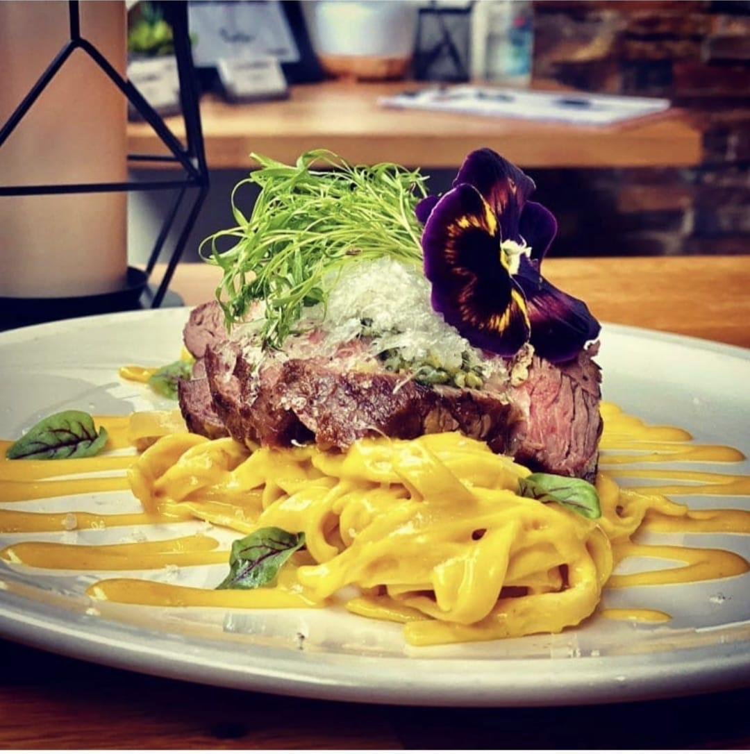 Seared steak over saffron cream tagliatelle with pea shoots and an edible flower